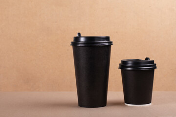 Two black paper cups of coffee or tea on cardboard background