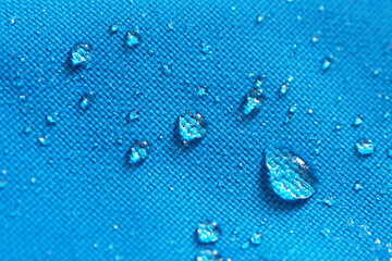Closeup of water drops on bright blue fabric with waterproof design to protect fabric of the cloth...