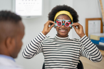Happy Young black woman checking vision with eye test glasses during a medical examination at the...