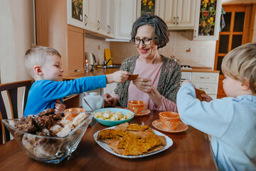 Grandchildren treat grandmother with cookies at the kitchen.