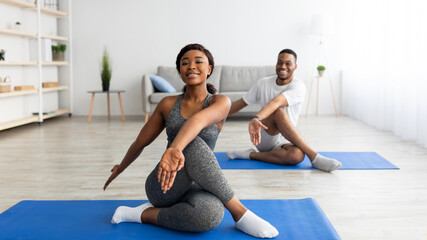 Flexibility exercises for healthier living. Athletic black couple doing yoga twist pose on home workout, copy space