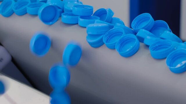 Many blue plastic bottle caps falling from conveyor belt at exhibition, factory - production line - close up. Manufacturing, recycling, industry, technology equipment concept