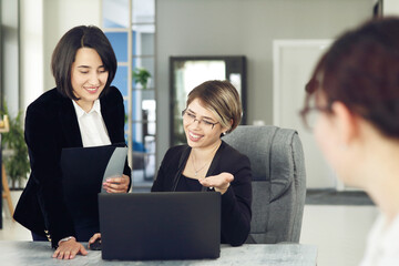 Two young business women in the office, analyzing information looking into a laptop and smiling