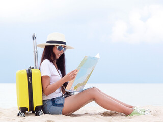 Summer Party. Traveler and tourism woman travel in summer on the beach and white sand. Asian is reading a map with yellow suitcase. On working in vacation concept.