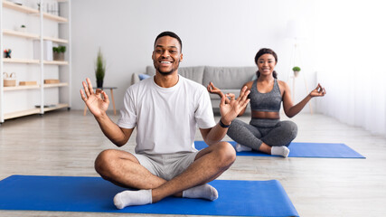 Happy black guy doing yoga practice with his girlfriend, sitting in lotus pose, making gyan mudra...