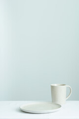vertical image of empty circle ceramic plate and ceramic mug placed on white tablecloths against white wall
