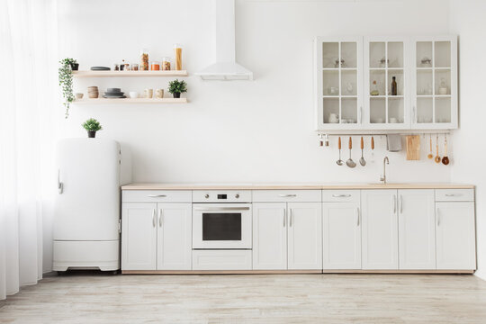 Minimal light scandinavian kitchen interior. White furniture with utensils, shelves with crockery, small refrigerator