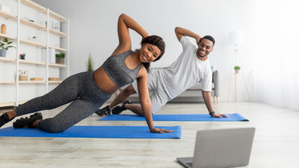 Online sports during covid lockdown. Fit black couple doing exercises in front of laptop at home, copy space