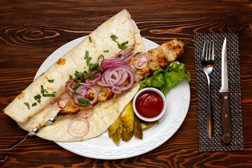 Chicken barbecue on a white plate on a dark wooden table with a knife and fork.