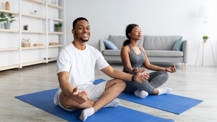Full length of young black couple meditating in lotus pose at home, empty space - obrazy, fototapety, plakaty