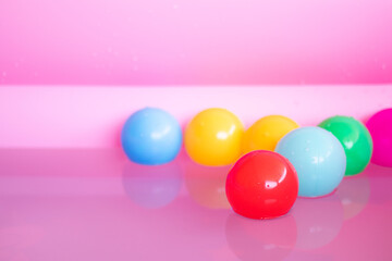 Several colored plastic balls float on the water in a pink tub.