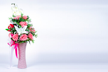 A beautiful bouquet of flowers in a pink vase placed on a table with a white backdrop and empty space to fill the message.