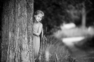 Little girl peeking from behind the pine trees in the Park. Black and white photo.