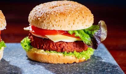 Tasty vegetarian food, homemade cheeseburgers made from plant based soya meat with cheese, onion, green lettuce and tomatoes