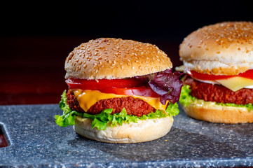 Tasty vegetarian food, homemade cheeseburgers made from plant based soya meat with cheese, onion, green lettuce and tomatoes
