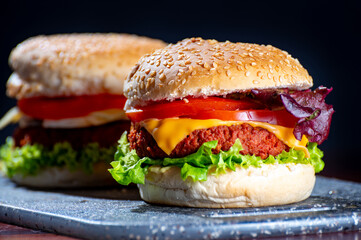 Tasty vegetarian food, homemade cheeseburgers made from plant based soya meat with cheese, onion, green lettuce and tomatoes