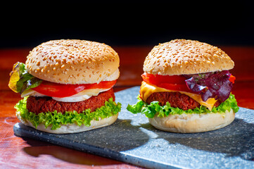 Tasty vegetarian food, homemade cheeseburgers made from plant based soya meat with cheese, onion, green lettuce and tomatoes