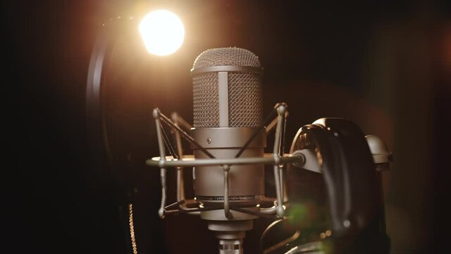Podcast, radio, interview, music studio recording. Close-up of microphone on stage against a black background with lighting. Silhouette of the microphone in the dark. Music instrument concept
