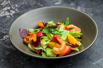 salad with shrimp, avocado, orange and strawberries on black plate on dark concrete table