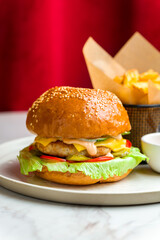 Burger with chicken, cheese and vegetables with french fries and ketchup on marble table and red curtain at the back