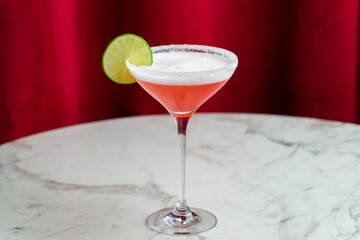 cosmopolitan cocktail with lime and salted rim on marble table and red curtain behind