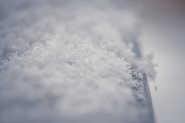 Tiny snowflake closeup on a handrail. Macro photography of winter. Crystal shaped flakes. Cold weather. Selective focus on the details, blurred background.