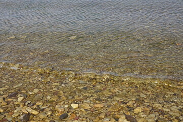 Yellow and brown colors pebble stones' backdrop on the beach in transparent water with a wave coming on a sunny day