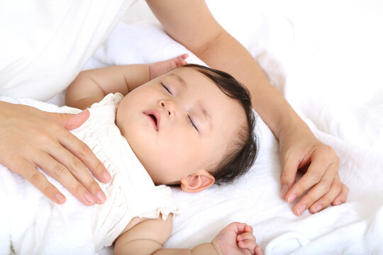 白背景で昼寝する赤ちゃんを見守るお母さん。育児、母性、愛情イメージ