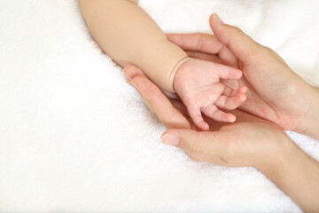 Mother's hand gently wrapping baby's hand on white sheets 