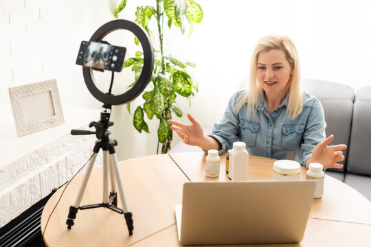 Blogger Woman Recording Video On Smartphone And Lighting Herself With Ring Lamp At Table In Light Room