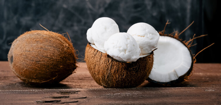 Fresh sweet coconut ice cream in a coconut shell on a wooden table. Sweet summer food.Wide banner.