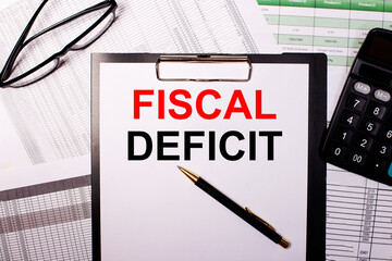 The words FISCAL DEFICIT is written on a white sheet of paper, near the glasses and the calculator.