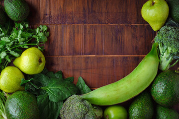 Fresh green vegetables around a wooden table. Tropical vegetables and fruits