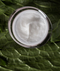 A jar of balm for hair on a background of foliage.
