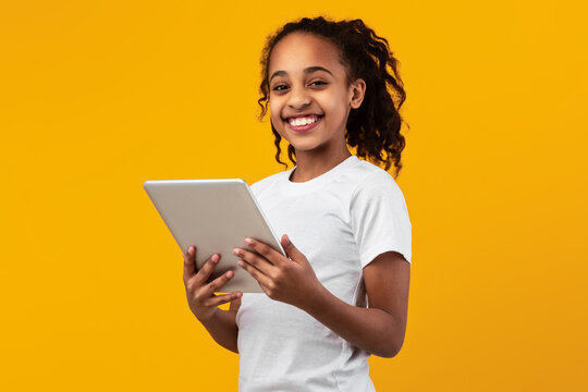 Black girl standing with tablet at yellow studio