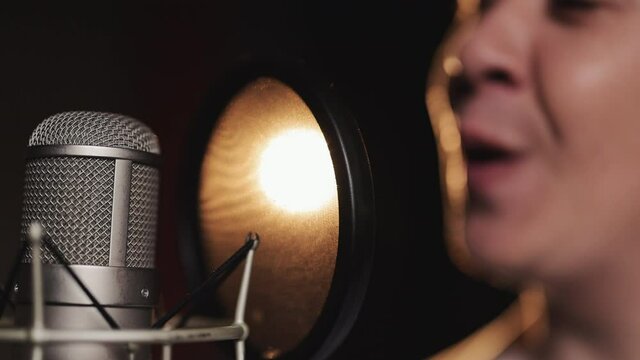 Close up of young professional male singer wearing headphones is performing a new song with a microphone while recording it in a music studio