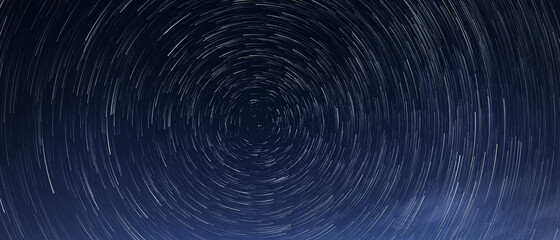 Stellar trails, the rotation of bright stars at night around the Polar Star against a blue sky 