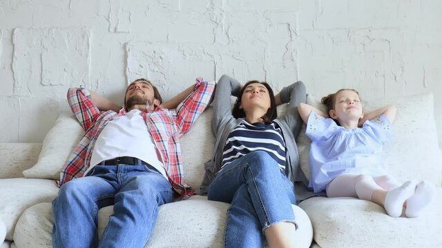 Relaxed young family resting and dreaming about new home on comfortable sofa together at home, happy young parents with little daughter relax enjoying nap relaxing or meditating.