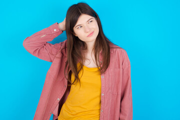 Fototapeta premium young beautiful Caucasian woman wearing pink T-shirt over blue wall saying: Oops, what did I do? Holding hand on head with frightened and regret expression.