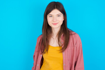 Fototapeta premium Happy young beautiful Caucasian woman wearing pink T-shirt over blue wall looking at camera with charming cute smile.