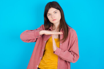 young beautiful Caucasian woman wearing pink T-shirt over blue wall feels tired and bored, making a timeout gesture, needs to stop because of work stress, time concept.