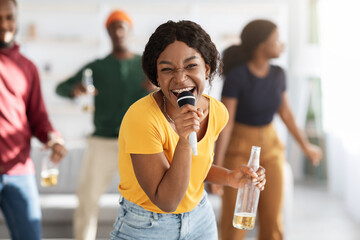 Laughing african american lady with bottle of beer singing karaoke