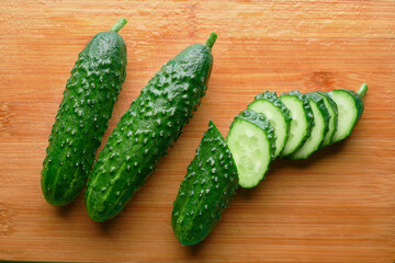 Set of fresh whole and sliced cucumbers on a wooden board with water drops. Garden cucumber wallpaper backdrop design