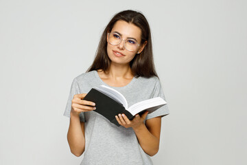 Fototapeta premium Beautiful woman in casual clothes and glasses reading book. Gray background. Free space for text.