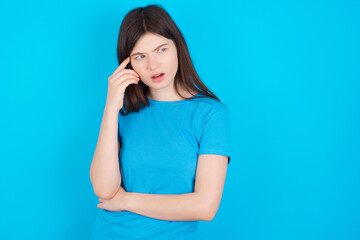 Fototapeta premium Astonished young beautiful Caucasian woman wearing blue T-shirt over blue wall looks aside surprisingly with opened mouth.