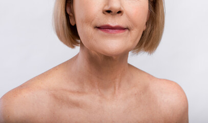Mature skin care concept. Cropped view of senior woman's face with bare shoulders on light studio background, closeup
