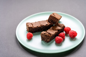 Home baked slices of chocolate brownies and raspberries on a round green plate 