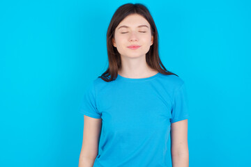 Fototapeta premium young beautiful Caucasian woman wearing blue T-shirt over blue wall nice-looking sweet charming cute attractive lovely winsome sweet peaceful closed eyes