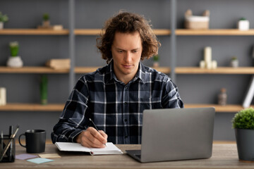 Serious Man Taking Notes Sitting At Laptop Computer In Office