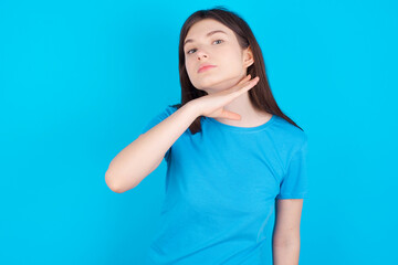 young beautiful Caucasian woman wearing blue T-shirt over blue wall cutting throat with hand as...